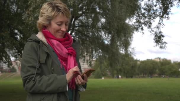 Vuxen kvinna med smartphone i parken — Stockvideo