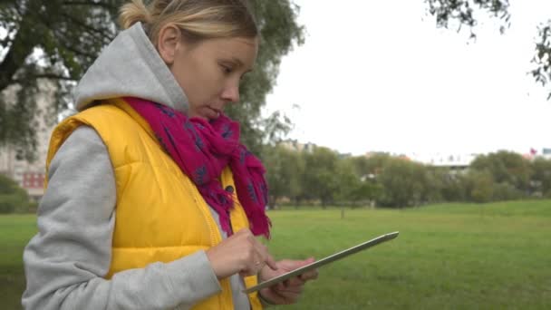Жінка в жовтому жилеті, використовуючи планшетний ПК в парку — стокове відео