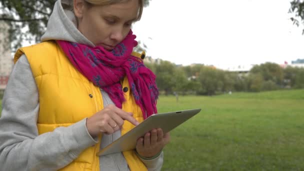 Mujer en chaleco amarillo usando tableta pc en el parque — Vídeos de Stock