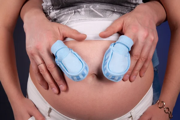 孕妇的肚子，与父亲的手和小蓝色的鞋子 — 图库照片