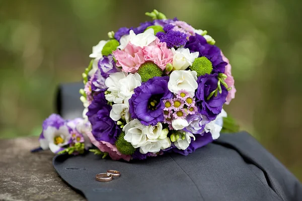 Wedding bouquet of eustomas lying on the jacket with rings — Stock Photo, Image