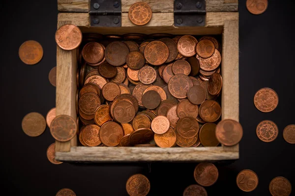 In the picture you can see a small wooden treasure chest in which you can see many different coins that are also scattered around