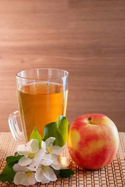 Apple juice in a glass, apple and apple-tree flowers on a wooden background. — Stock Photo, Image