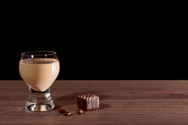 Glass with liquor, candy and coffee beans on a black background.
