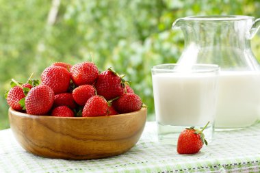 Strawberries in a wooden bowl, a glass and a jug of milk.