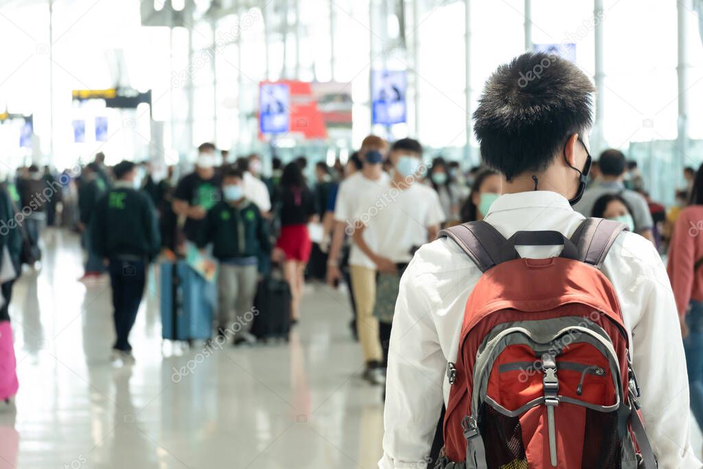 Asian traveler man wearing face mask waiting to board into airplane, standing in departure terminal in airport