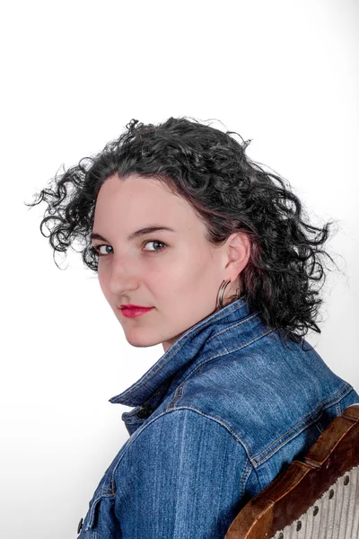 Young model in her mid twenties sitting on a wooden chair with a blue denim jacket. — Stock Photo, Image