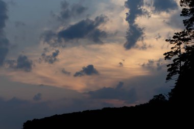Karanlık bir gökyüzüne karşı büyük kabarık bulutlar. Doğada gün batımı