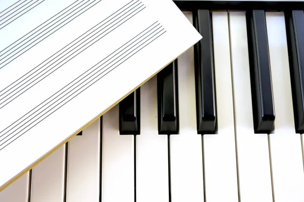 ノートのノートブックは シンセサイザーを演奏する音楽シート音楽を学ぶ黒と白のピアノキーにあります — ストック写真