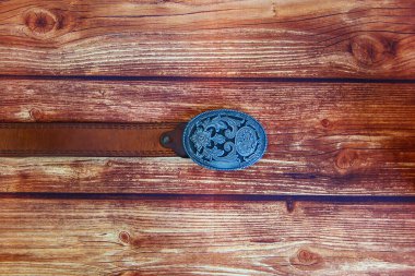 Deri kovboy kemeri ve ahşap arka planda oval desenli toka.