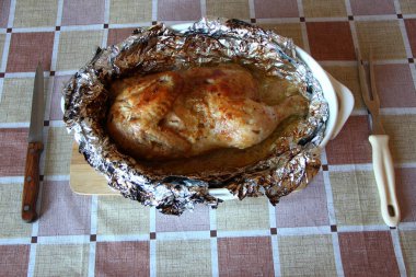 Çatal ve bıçakla folyoda pişmiş yarım tavuk.