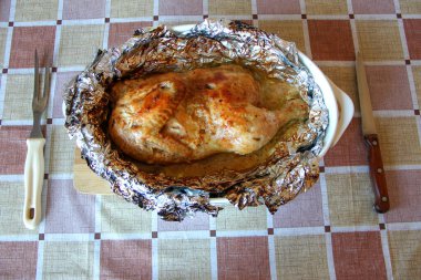 Çatal ve bıçakla folyoda pişmiş yarım tavuk.