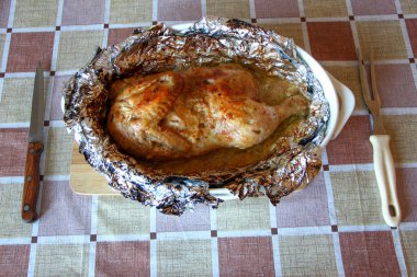 Çatal ve bıçakla folyoda pişmiş yarım tavuk.