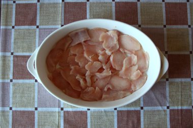 Seramik fırın kabında dilimlenmiş çiğ tavuk göğsü.