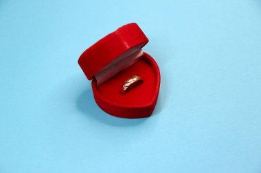 Altın yüzük. Kırmızı kadife kutu. Mavi arka planda kalp şeklinde.