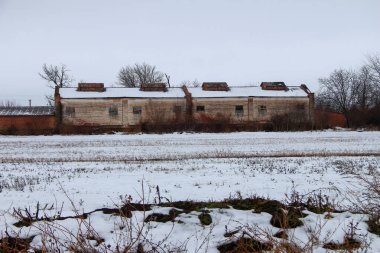 Terk edilmiş eski çiftlik, karlı tarla ve arka planda elektrik direkleri.