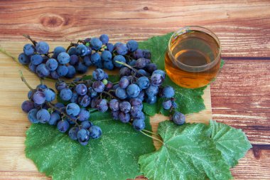 Kahverengi ahşap zemin üzerinde yapraklı mavi üzüm demetleri ve bir bardak şarap.