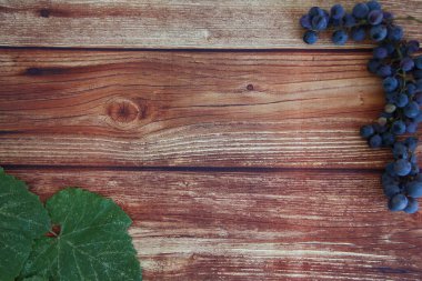 Kahverengi ahşap zemin üzerinde yaprakları olan mavi üzüm demetleri.