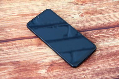 Ahşap arka plana yansıyan tuğla duvarlı siyah ekranlı akıllı telefon.