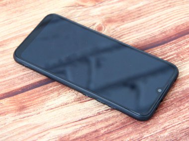 Ahşap arka planda baş aşağı duran siyah akıllı telefon.
