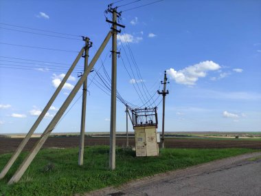 Kırsalda eski trafo kutusu ve elektrik hatları var.