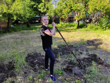 Çapalı genç bir kadın sebze bahçesinde çalışıyor.