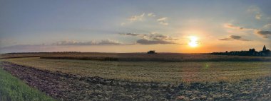 Panorama, tarım alanında bir biçerdöver ile batan güneşin arka planına karşı.