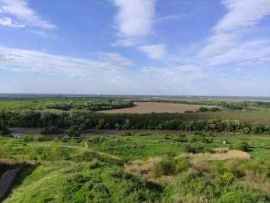 Ormanı, nehri ve bulutlu mavi gökyüzü olan güzel bir yaz vadisi.