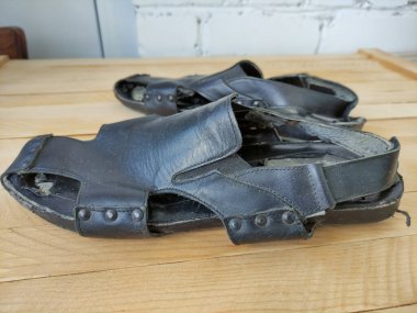 Ahşap arka planda pejmürde siyah erkek sandaletleri.