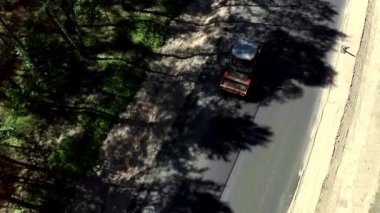 Ormandaki boş bir yolda giden bir yol silindirinin hava görüntüsü.