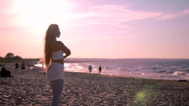 Jonge atletische vrouw stretching bij zonsondergang op het strand — Stockvideo