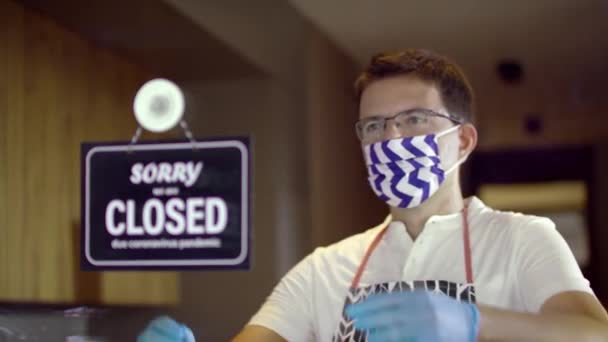 Snygg vit arbetare bär en skyddande ansiktsmask vända över stängd för att öppna skylt på fönstret på grund av pandemi — Stockvideo