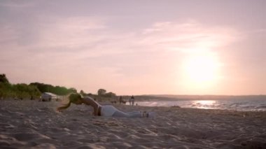 Genç Atletik Kadın plajda gün batımında Burpies yapıyor.