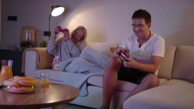 Rekabetçi çiftler evlerinde video oyunları oynarken birbirlerini itip kakıyorlar.