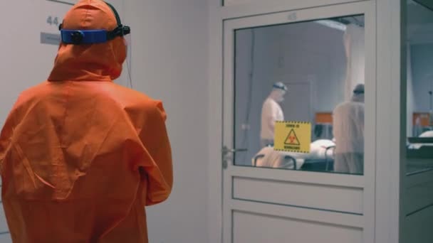 Médico en un traje naranja entra en la sala de aislamiento con pacientes con Coronavirus — Vídeo de stock