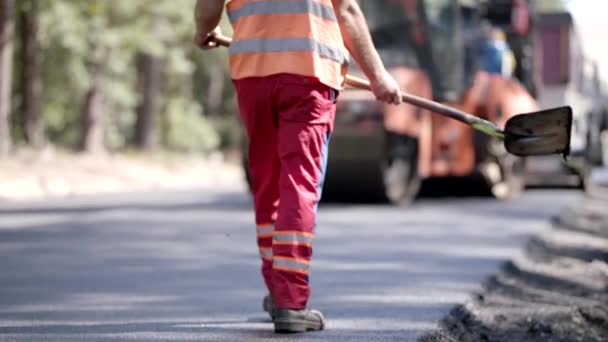 Trabajador de la construcción de carreteras está caminando con una pala en una carretera asfaltada — Vídeos de Stock