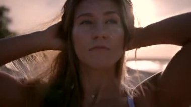 Genç bir kadın, COVID-19 salgını sırasında kumsalda güneş batarken saçını düzeltiyor.