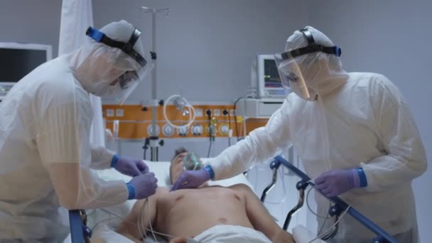 Slowmo - Lékaři v ochranných oblecích navázání EKG vodítek na pacienta s koronavirem — Stock video