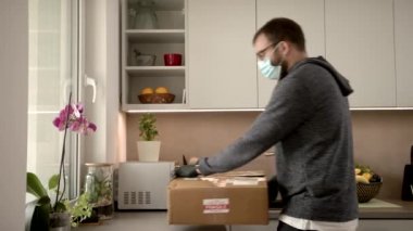 Yetişkin, mutfağa salgın hastalık taşıyan bir COVID 19 paketi getiriyor ve açıyor.