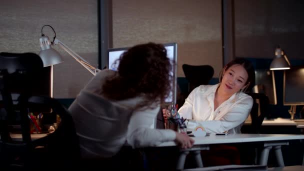 Молодые профессиональные женщины разговаривают и улыбаются во время работы допоздна — стоковое видео