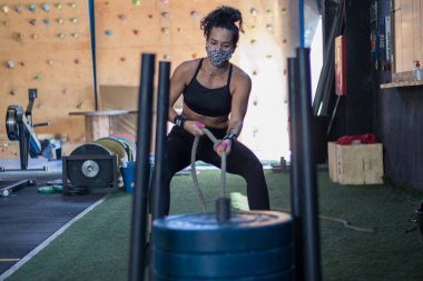 Spor salonunda maske takan kız Cross antrenmanı yapıyor.