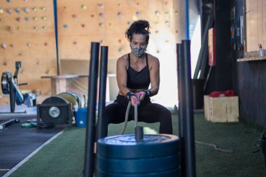 Spor salonunda maske takan kız Cross antrenmanı yapıyor.