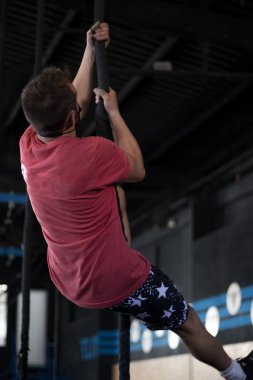 Spor salonunda maskeli bir çocuk çapraz antrenman yapıyor, ip tırmanışı yapıyor.