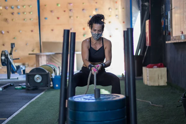 Spor salonunda maske takan kız Cross antrenmanı yapıyor.
