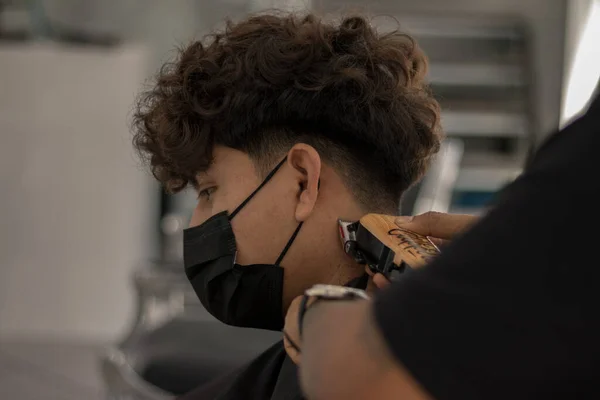 在发廊里和一个年轻的理发师一起 带着面具 在大流行的时候给一个戴面具的男孩剪头发 — 图库照片