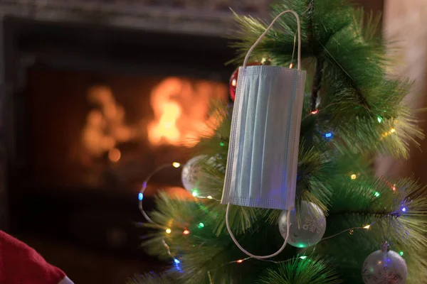 Mask hanging on a Christmas tree with the fireplace lit in the background