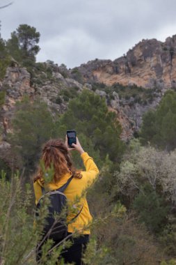 Woman from behind with a yellow jacket sits on a rock on top of a mountain in autumn with mist