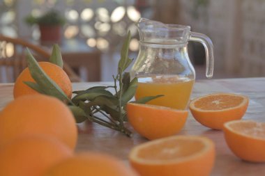 Doğa ile çevrili bir kır evi masasının üzerinde portakal suyu dolu cam sürahi.