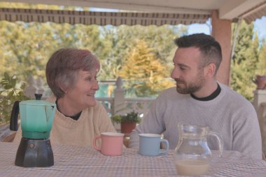 Anne ve oğlu, doğayla çevrili bir kır evinin terasında İtalyan bir kahve makinesiyle yapılan lezzetli kahvenin tadını çıkarıyorlar.