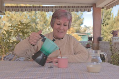 Doğayla çevrili bir kır evinde İtalyan bir kahve makinesinden kahve içen bir kadın.